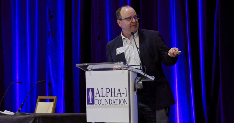 speaker standing at podium featuring Alpha-1 Foundation logo