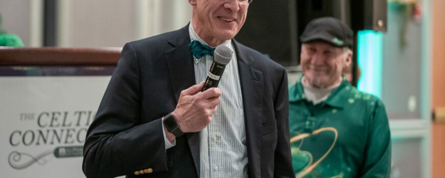 speaker in a suit holding a microphone and smiling