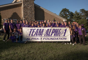 group of people outside in Alpha-1 purple t-shirts holding "Team Alpha-1" banner